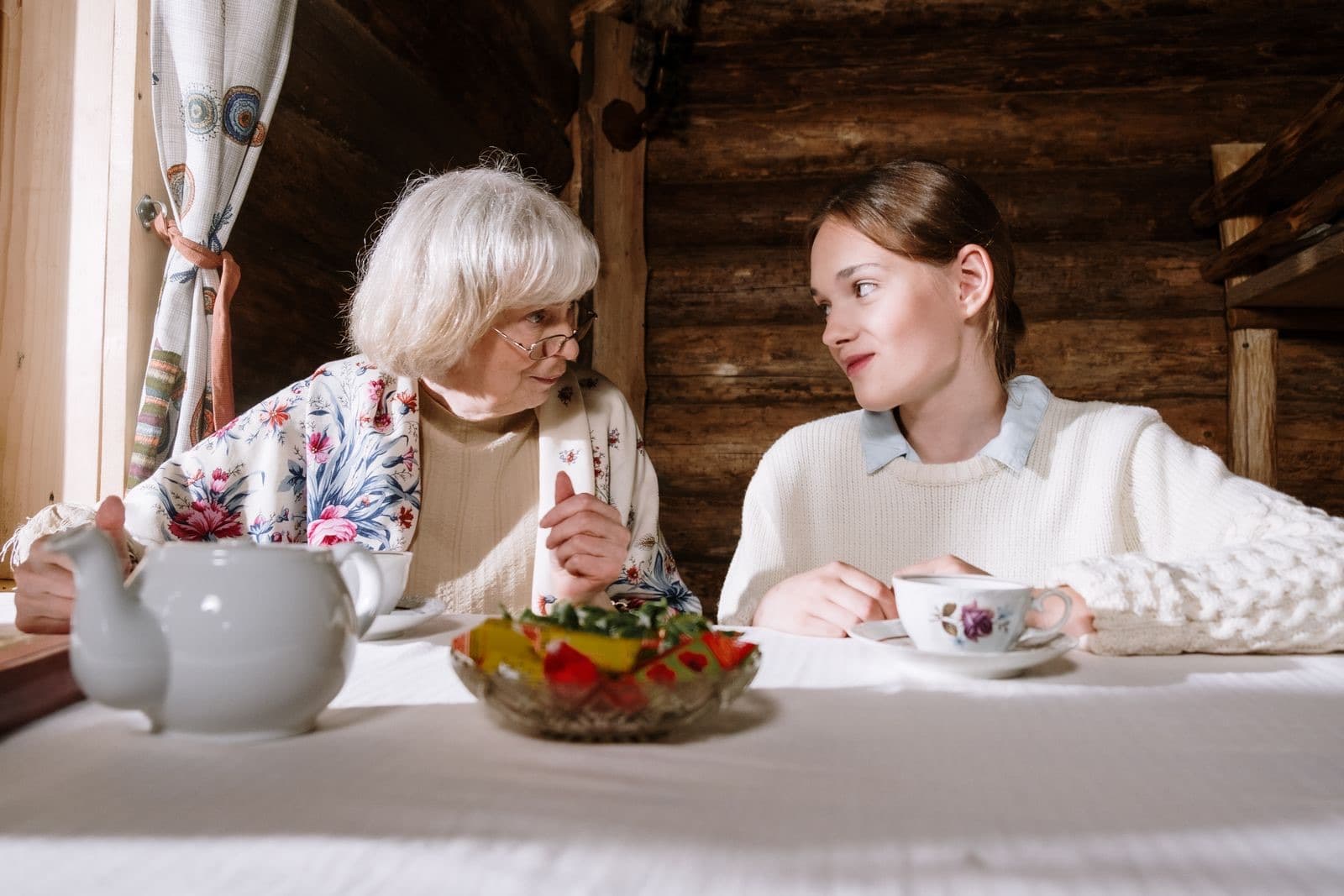 An older woman and a young woman talking over cups of tea at a kitchen table