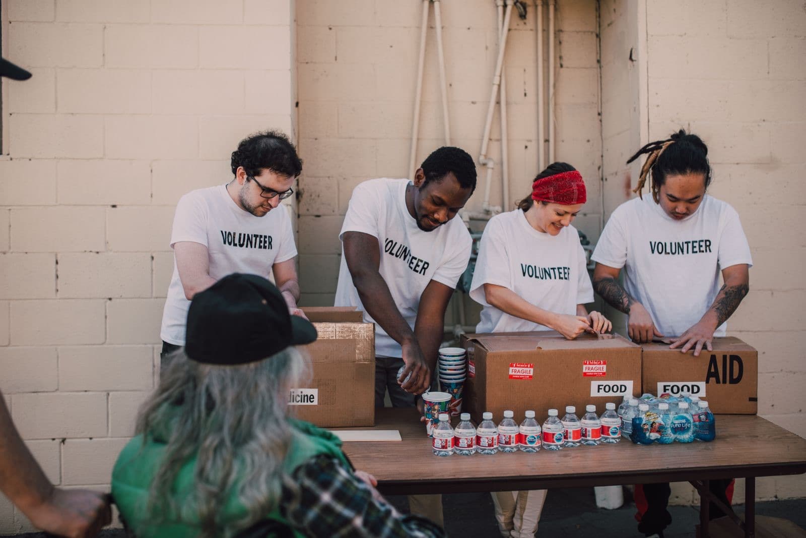 Four people in matching T-shirts packing boxes of food, water and supplies at an outdoor table